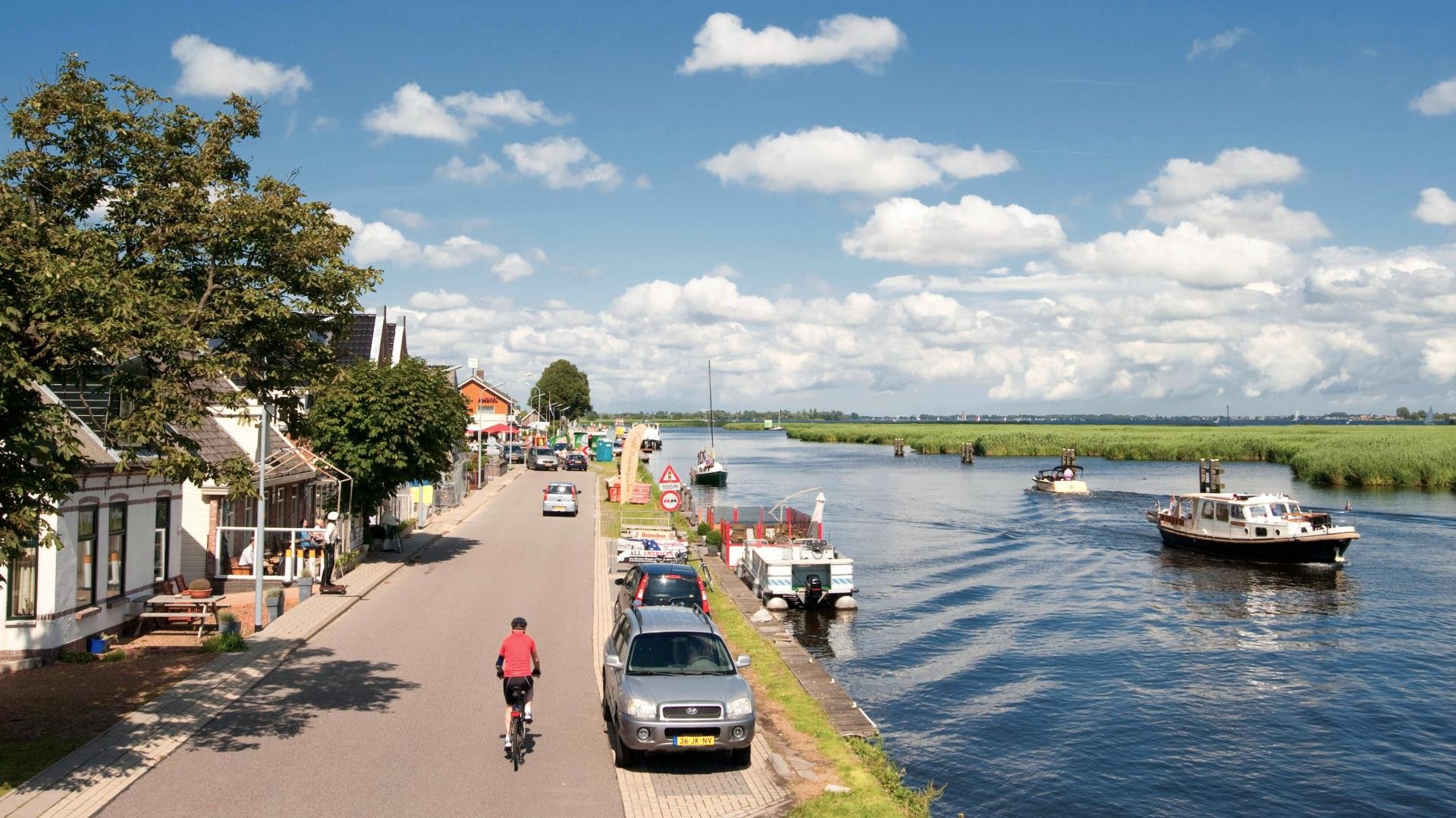 Afbeelding: headerfoto Ringdijk en Ringvaart op zonnige zomerdag met fietser, geparkeerde auto's en boot op het water.