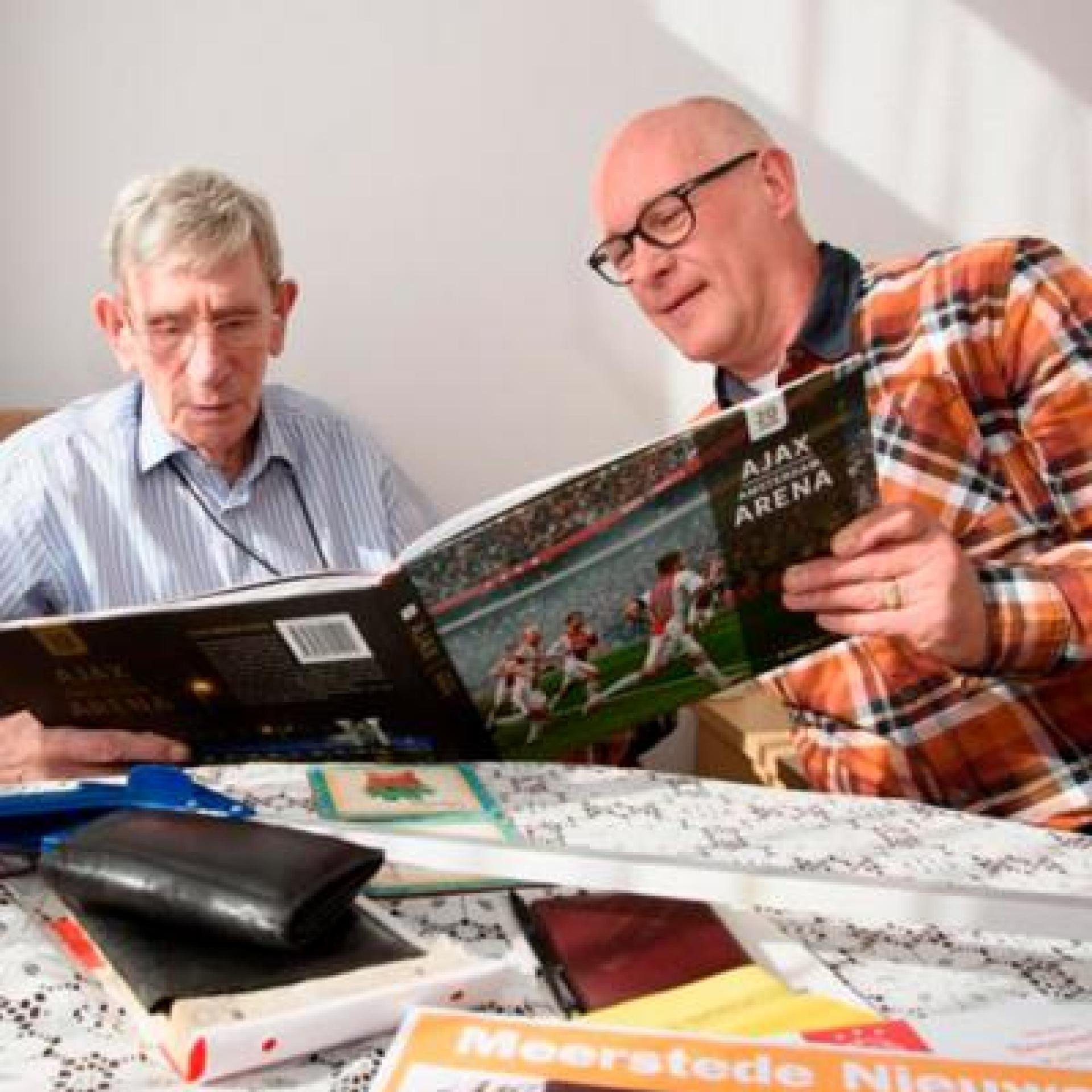 Afbeelding: foto van vrijwilliger Gerrit en maatje Gerrit, samen bekijken ze een voetbalboek
